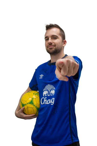 A man wearing the blue Everton Football Club home shirt. He is holding a yellow ball under his arm and pointing at the camera. 