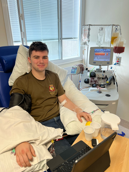 a young man in a hospital bed, he is wearing a grey t-shirt and he is smiling