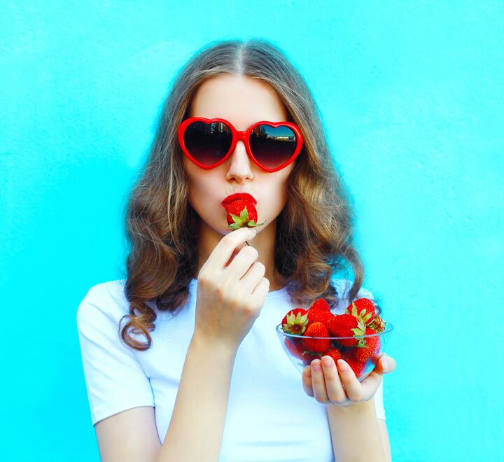A woman with sunglasses eating a strawberry