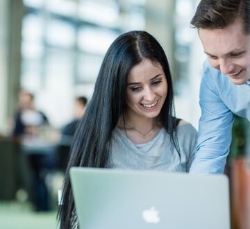 En jente med langt svart hår sitter, smilende og jobber på en pc