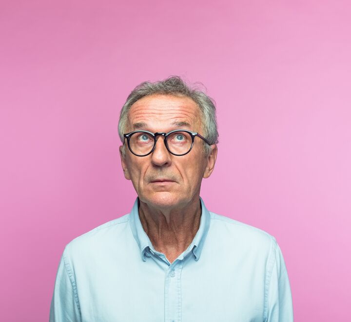 Usikker og tankefull mann foran rosa bakgrunn.