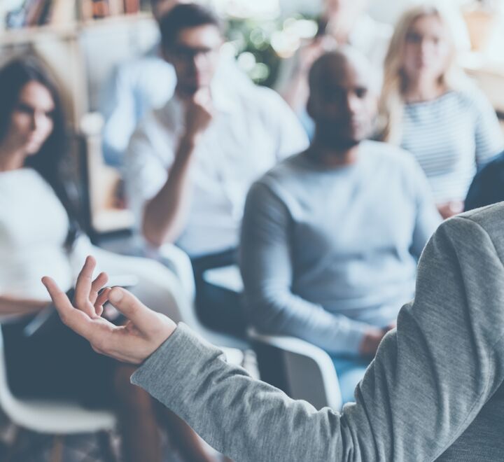 Image of a workshop group where one person is standing in front and presenting in front of the rest.
