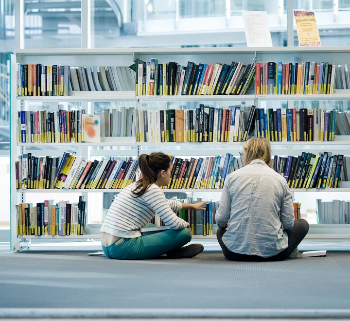 Two students searching through a bookshelf.
