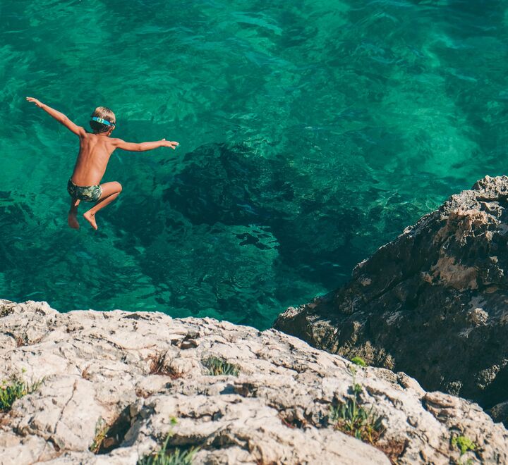 Gutt hopper fra en klippe og ned i vannet