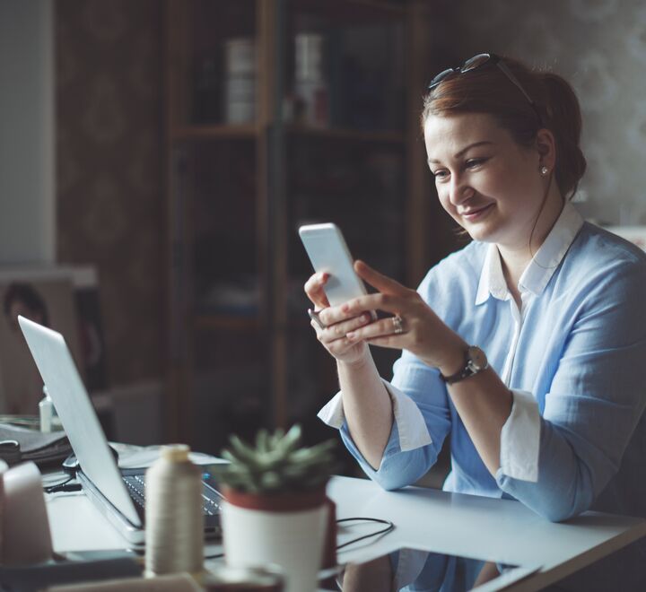 Woman working from her desk at home, using her phone.