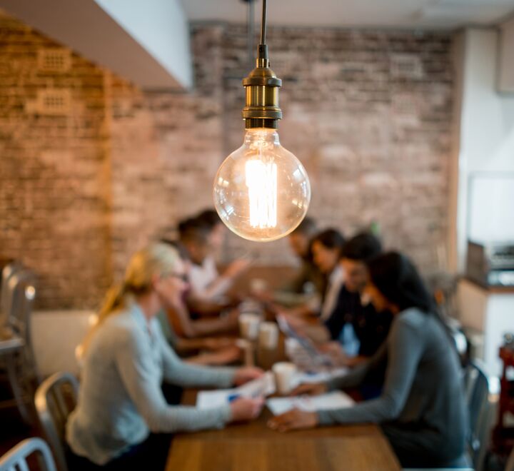 Group of students working together. A light bulb hanging from the roof in focus.