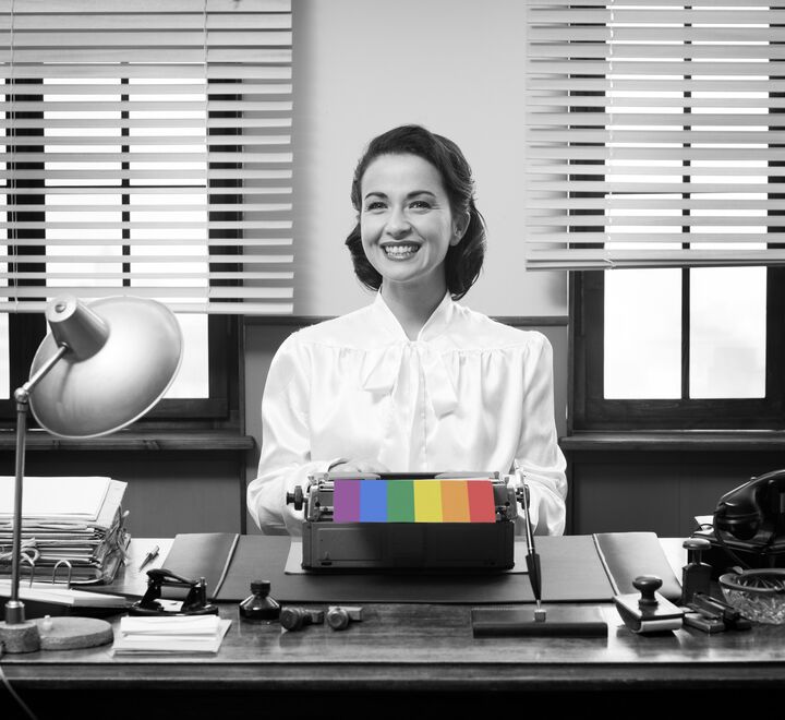 Black and white image of female office worker with rainbow coloured paper coming out of her typewriter