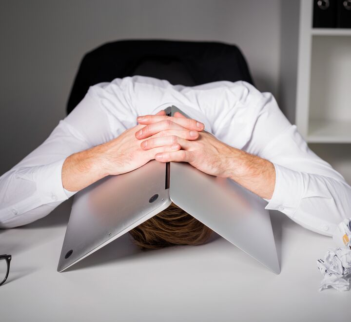 Frustrert mann gjemmer seg under en laptop
