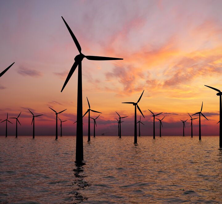 Wind turbines in the ocean. Sun set in the background with orange colours.