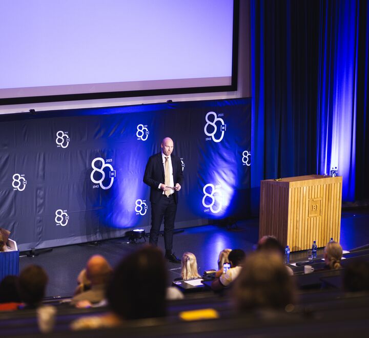 Person som står på scenen og snakker under Alumnidagen 2023