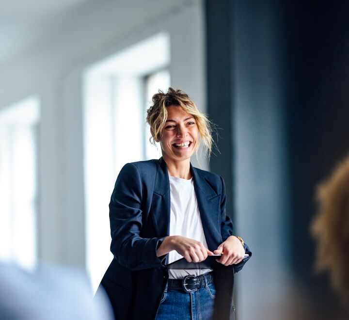 Kvinnelig kollega smiler og holder en presentasjon for sine kolleger.