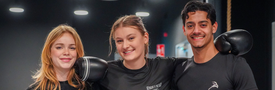 Drie lachende studenten, arm in arm na een bokstraining.