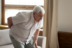 Senior grey haired 70s years man got up from couch writhes in pain felt sharp ache suffers from low back strain, touch loin reduce backache. Degenerative disk disease, pinched nerve rheumatism concept