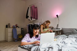 Two multiracial girls listening music and using laptop while spending time together at home