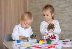 Little children paint with paints. The kids got their hands dirty in gouache. A cute girl and a boy with Down Syndrome are creative.
