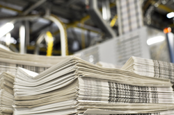 stack of freshly printed daily newspapers transported to a printing plant, in the background machines and technical equipment of a large printing plant 