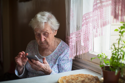 An old woman sits with a smartphone in her hands in the home Shutterstock ID 1710455221