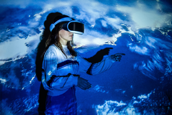 Woman using virtual reality headset, moving hand at interactive technology exhibition with multicolor projector light illumination, immersive concept