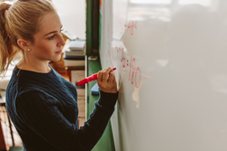 Close up of female student writing an equation on white board in classroom. Girl writing on board during maths class.