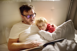 Father reading bedtime stories to child. Dad putting son to sleep. Quality family time.