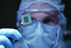 In Ultra Modern Electronic Manufacturing Factory Design Engineer in Sterile Coverall Holds Microchip with symbols in futuristic holography. artificial intelligence, future of robots.
