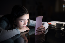 Sad female checking smart phone content in the dark night at home