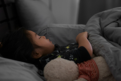 Asian child cute or kid girl sleeping well with comfortably and sweet dream at night for relax on gray dark bed and pillow blanket with teddy bear doll in bedroom at home and morning to wake up late