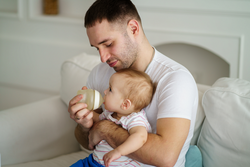 father feeding his little son from bottle. toddler boy and dad in living room. babysitting, childcare, parental leave, fatherhood, parenting