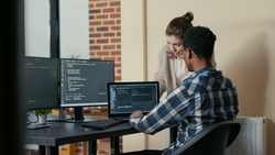 Two programmers doing high five hand gesture at desk with multiple screens running code celebrating successful algorithm. Software developers colleagues enjoying teamwork results in it agency