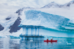 winter kayaking in Antarctica, extreme sport adventure, people paddling on kayak near iceberg