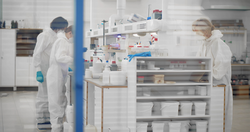 Chemists in modern laboratory doing research during global epidemic with covid-19. Scientific team wearing respirator mask and protective overall working in biochemical lab