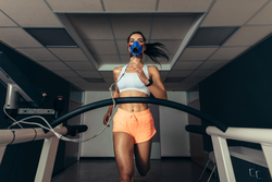Fit young woman running on treadmill with a mask. Athlete examining her performance in sports science lab.