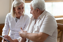 Elderly 80s man patient and middle-aged nurse medical worker holding clipboard writing personal information having pleasant warm conversation talk with clinic client nursing caregiving service concept