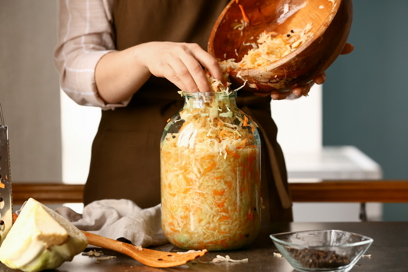 Woman putting tasty sauerkraut into glass jar on table in kitchen, closeup