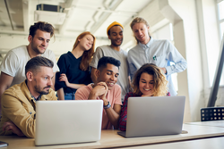 Group of millennial male and female colleagues collaborating on startup project browsing web publication on modern laptop computers, happy colleagues enjoying brainstorming meeting in coworking