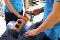 Electrostimulation, treatment and rehabilitation. Physiotherapist doctor performs surgery on a patient's leg
