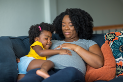 African American llittle girl holding her mother's stomach.