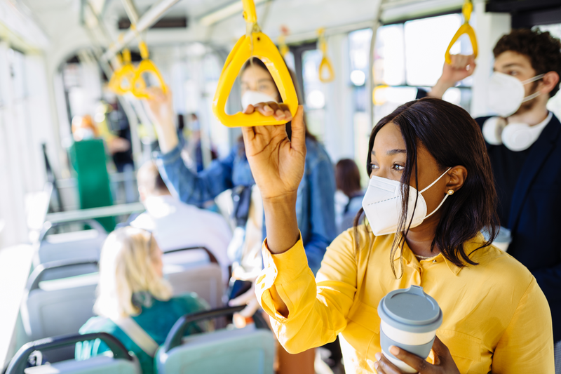 Pensive tired black woman commuting work by bus and wearing protective face mask due to coronavirus pandemic. Thoughtful african american girl holding handles in bus or subway train.