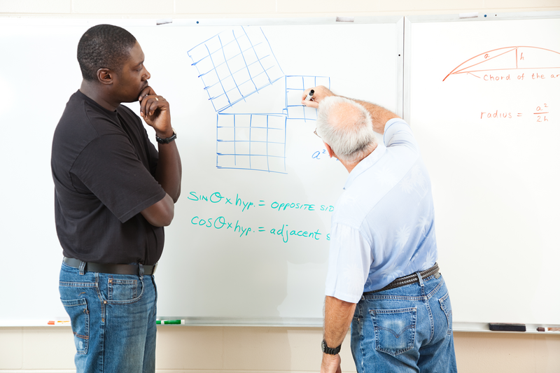Teacher and adult student at the board working trigonometry equations. Focus on the equations on the board.