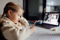 Caucasian kid studying online at home and using laptop. Distance or remote learning for child. Pretty stylish schoolgirl studying homework math during coronavirus covid-19 quarantine and social