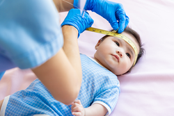 asian doctor measure baby head by tape to check-up his grow curve and infant lying on bed