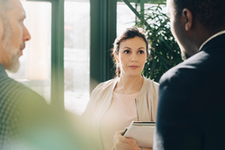 Serious businesswoman listening to male colleagues while standing in office