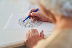 Elderly woman with pen solves a maze puzzle as a brain teaser and memory training against dementia