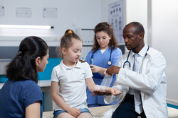 African american pediatrician doctor bandage broken arm of young child during medical appointment in hospital office. Girl patient with fractured hand having physiotherapy. Trauma recovery
